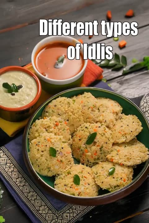 A green bowl filled with vegetable-loaded rava idlis, served with a bowl of orange sambar and white coconut chutney. The text Different types of Idlis is overlaid at the top in white.