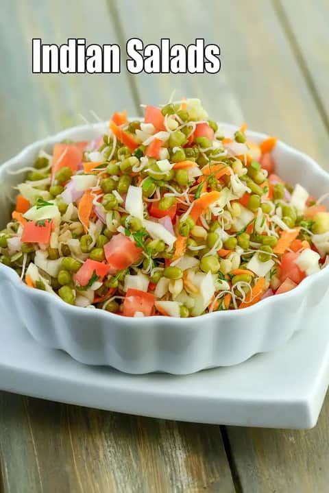 A bowl of Indian salad made with sprouted green moong, chopped tomatoes, carrots, cabbage, onions, and fresh herbs, served in a white bowl on a wooden surface.