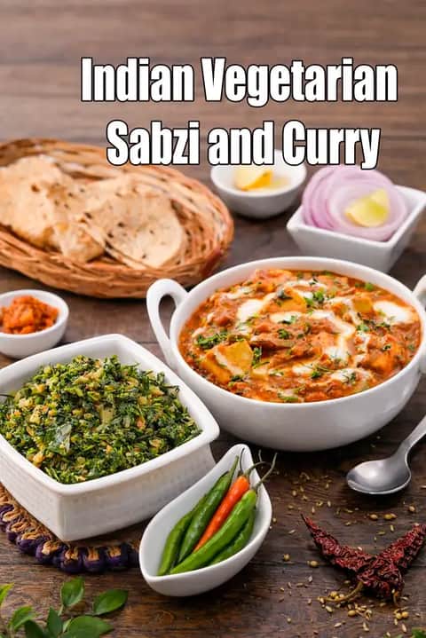 image of an Indian dining table with two vegetarian dishes placed neatly: a dry green leafy sabzi in a white square bowl and a rich paneer curry in a white serving bowl. The setup includes roti in a basket, sliced onions, lemon, green chilies, rice, and spices on a rustic wooden table.