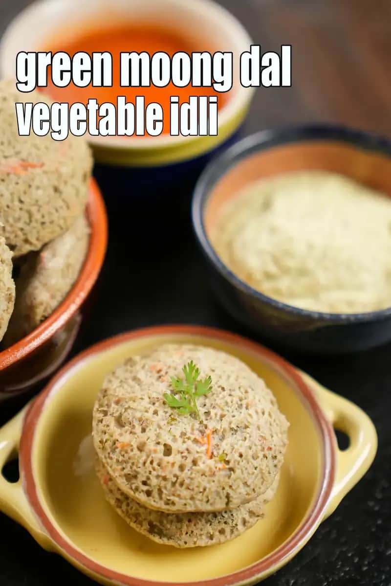 Green moong dal vegetable idli stacked in a yellow ceramic bowl, garnished with coriander, served with coconut chutney and red chutney in small bowls.