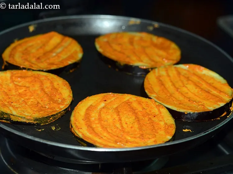 Step 11 – Arrange few baingan slices on the hot tava. You can also arrange half the baingan …
