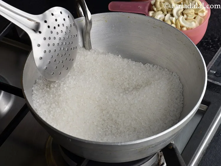 Step 4 – Add 1&frac12; cups of sugar to the kadhai. The sugar and cashew halves in this …