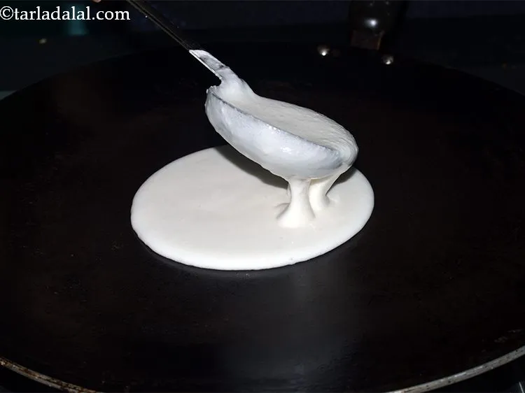 Step 38 – Pour a ladleful of the batter on the tava (griddle).