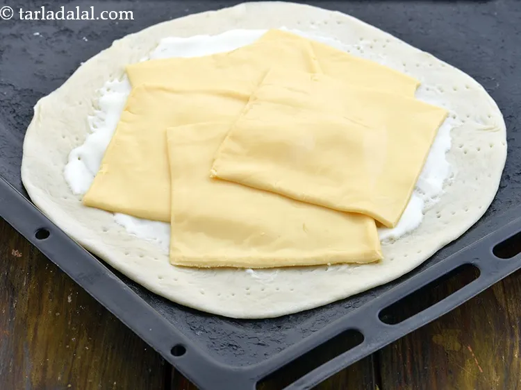 Step 26 – Place 5&nbsp;<a href="https://www.tarladalal.com/glossary-cheese-slices-765i">cheese slices</a>&nbsp;over the cheese spread, overlapping each other.
