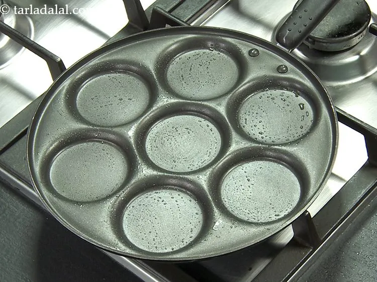 Step 12 – For making cucumber pancakes, heat a non-stick mini uttapam pan and grease it lightly using …
