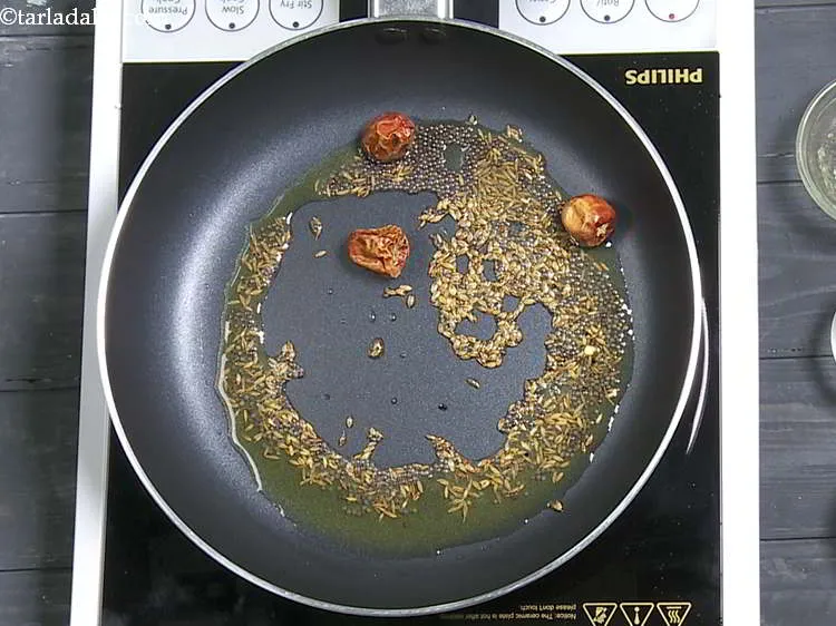 Step 7 – When the seeds crackle, add the round red chillies.