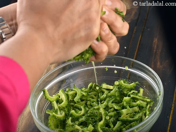 Step 7 – Squeeze out all the excess water by pressing the karela slices in between your palms …