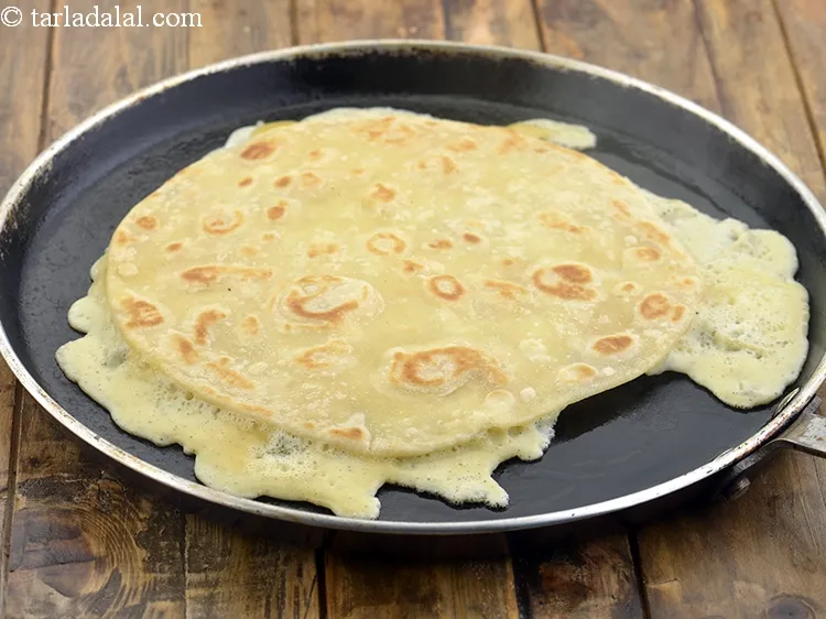 Step 26 – Pour the egg mixture on it and immediately place the cooked roti over it.