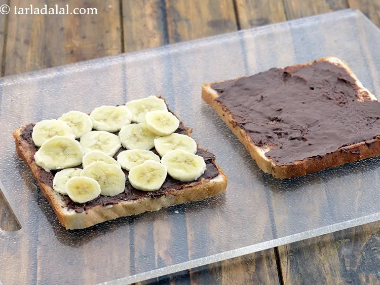 Step 6 – Place &frac14; cup of <a href="https://www.tarladalal.com/glossary-sliced-banana-19i">bananas slices</a>&nbsp;evenly over 1 buttered-nutella spread side.