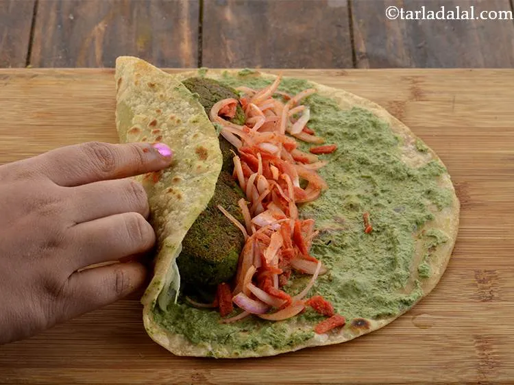 Step 42 – Roll up the left side of the roti and fold it over the&nbsp;<strong>Hara Bhara Tikkis</strong>.