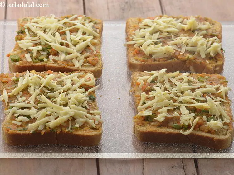 स्टेप 15 – प्रत्येक बटर ब्रेड स्लाइस पर १ टेबल-स्पून चीज़ छिड़कें। हमने …