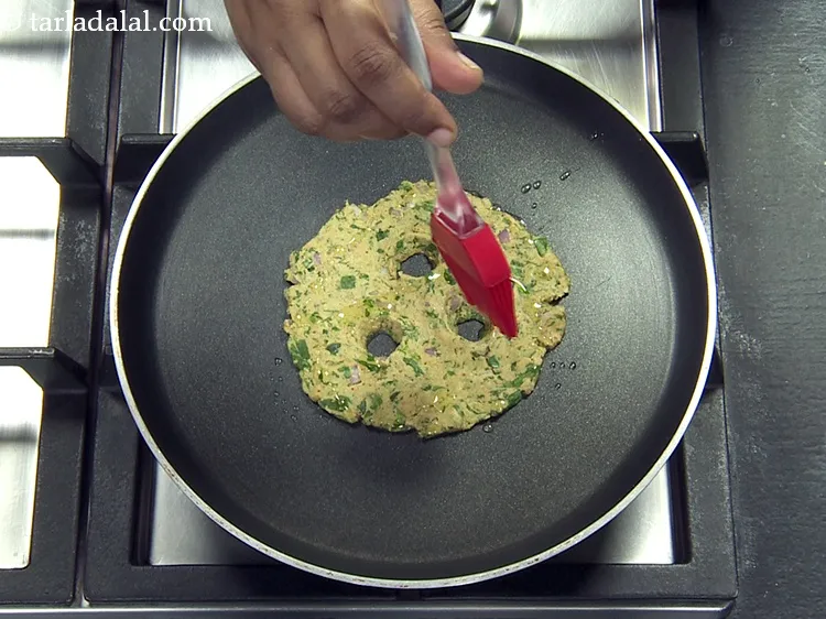 Step 42 – Spread 1 tsp of <a href="https://www.tarladalal.com/glossary-oil-671i">oil</a>&nbsp;all over the thalipeeth, including the holes made in the …