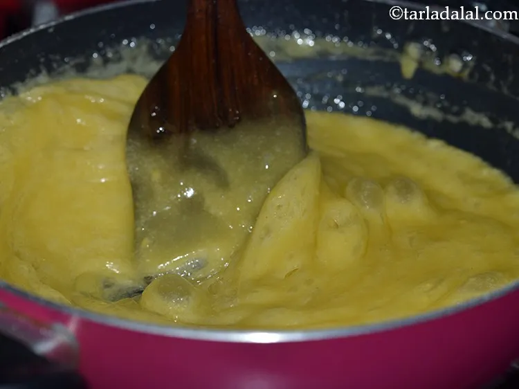 Step 15 – Keep mixing continuously using the ladle until the besan-sugar syrup mixture has absorbed all the …