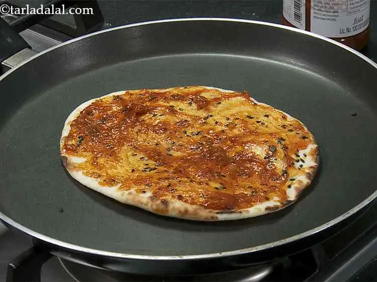 Step 18 – Place the <strong>naanza</strong> base on the tava, put 1 tbsp of pizza sauce on the …