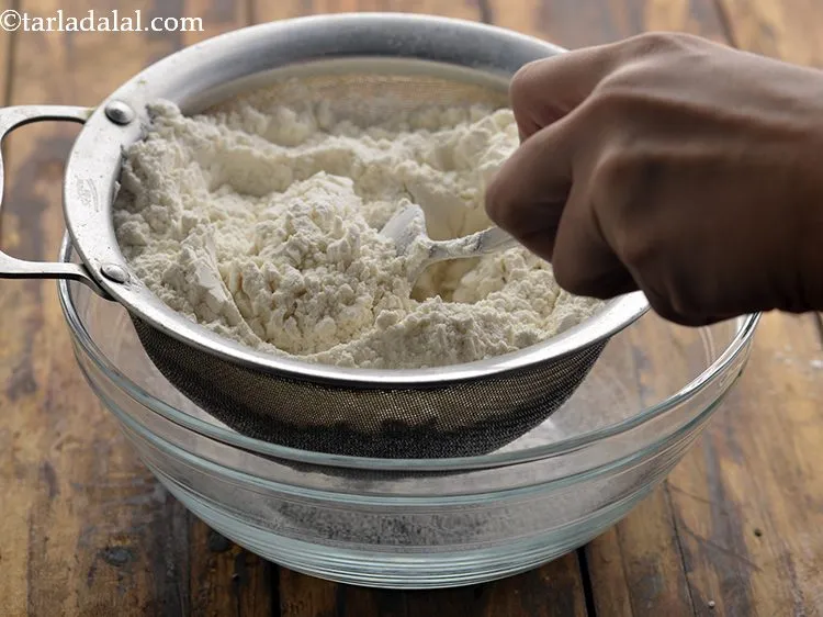 Step 2 – For making the&nbsp;<strong>Nankhatai Biscuit</strong>, in a deep bowl, place a fine sieve or strainer. Add …