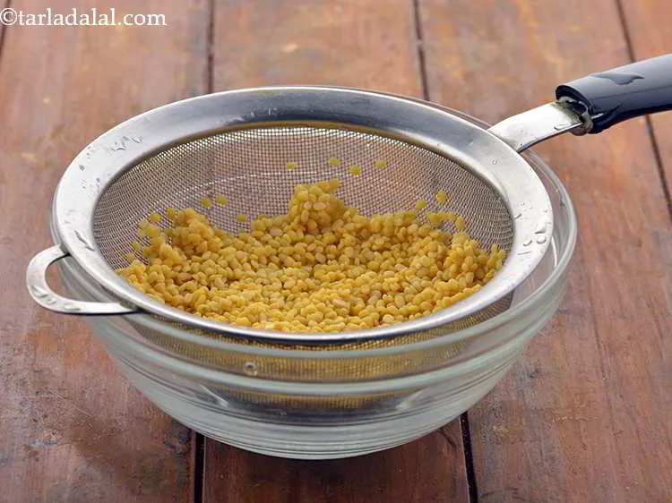 Step 8 – Take yellow <em>moong dal</em> in a strainer. Wash it 2-3 times under running water. Drain …