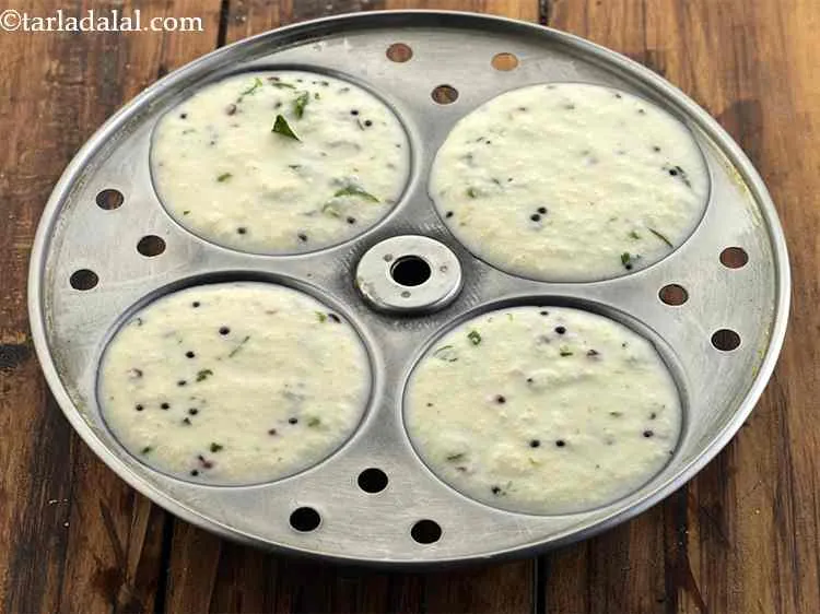 Step 18 – Pour a little tempering of&nbsp;<strong>Sooji Idli</strong>&nbsp;batter into each greased idli mould. Do not overfill the …