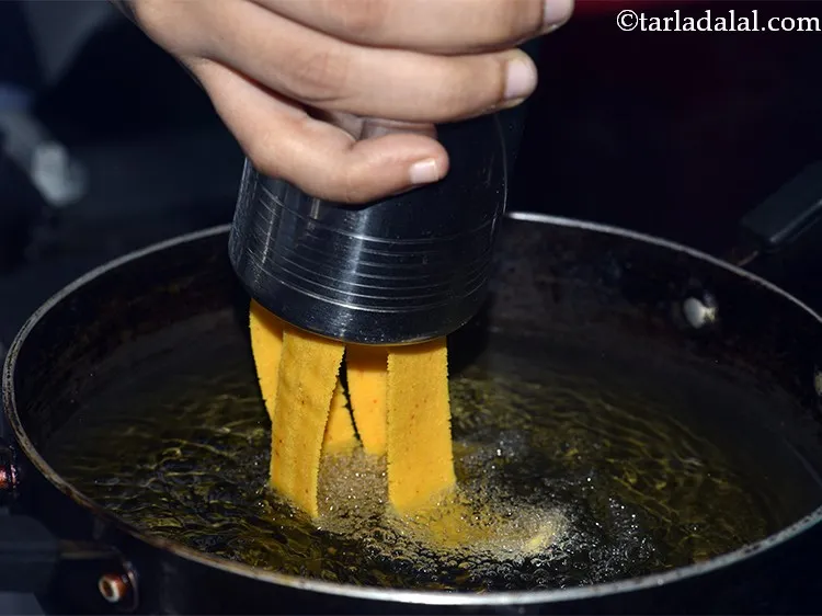 Step 13 – Hold the sev press over pan, turn the handle of machine and press out ribbons …