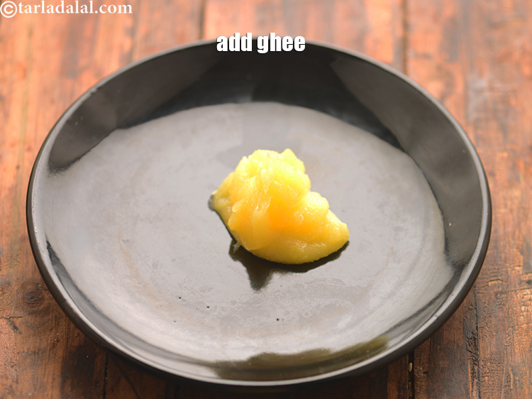 Step 14 – Take a big thali or plate and add 1 1/4 tbsp&nbsp;<a href="https://www.tarladalal.com/glossary-ghee-245i">ghee</a>. Here we have …