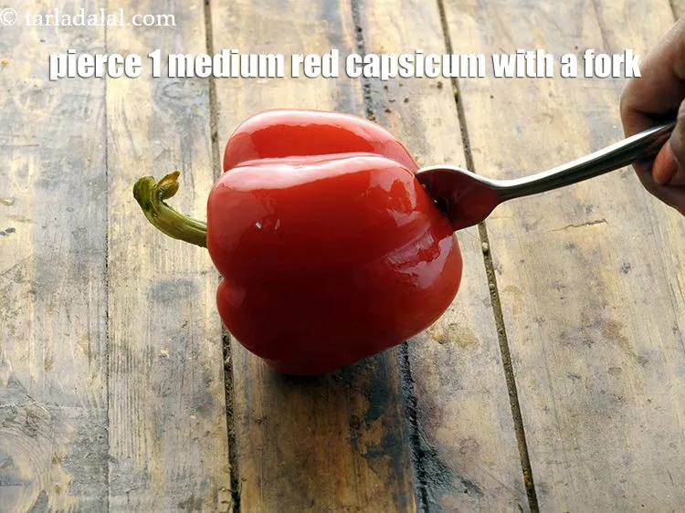 Step 13 – Pierce 1&nbsp;medium&nbsp;<a href="https://www.tarladalal.com/glossary-red-capsicum-red-bell-pepper-laal-shimla-mirch-172i">red capsicum</a> with a fork.