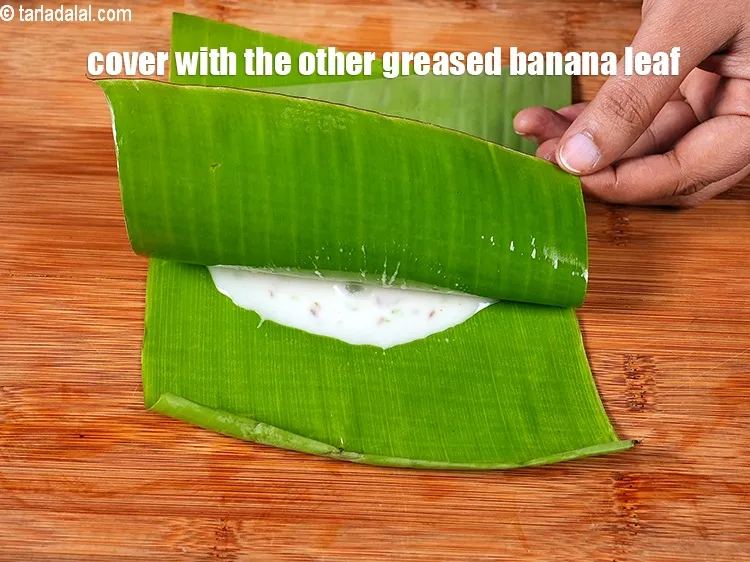 Step 18 – <meta charset="UTF-8" />Cover with the other greased banana leaf with the greased side facing downwards.&nbsp;&nbsp; …