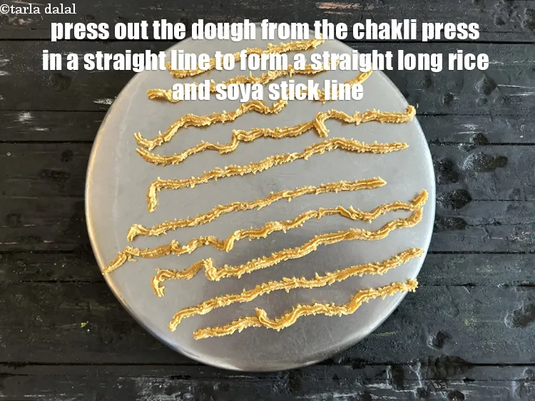 Step 18 – Press out the dough from the chakli press on the greased thali &nbsp;in a straight …