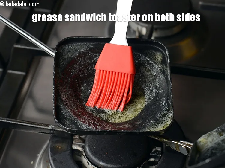 स्टेप 18 – सैंडविच टोस्टर को दोनों तरफ &frac12; टी-स्पून मक्खन लगाकर चिकना …
