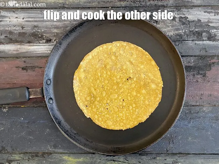 स्टेप 20 – <strong>खाखरा को</strong>&nbsp;पलटें और&nbsp; दूसरी तरफ से भी पकाएँ। धीमी आंच …