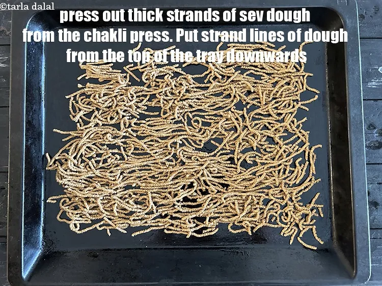 Step 20 – Press out thick strands of sev dough from the sev press &nbsp;onto a greased baking …