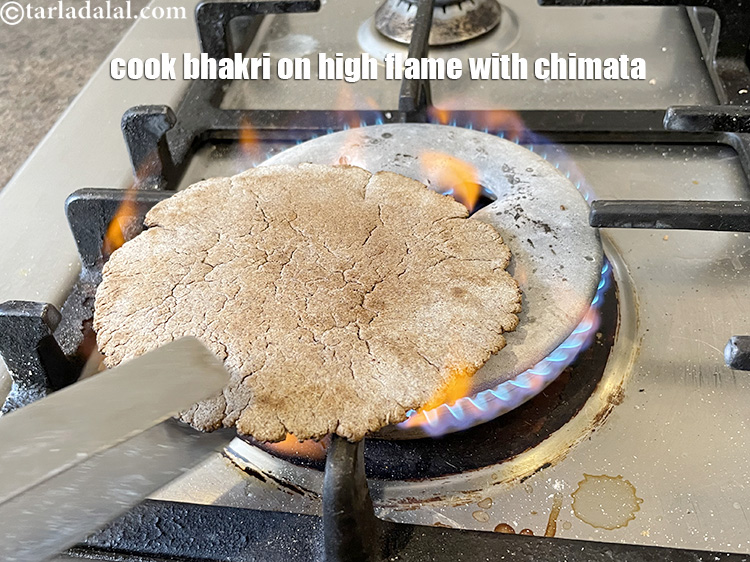 Step 11 – On a high flame, take a pair of tongs ( chimata) further &nbsp;cook the &nbsp;bhakari …