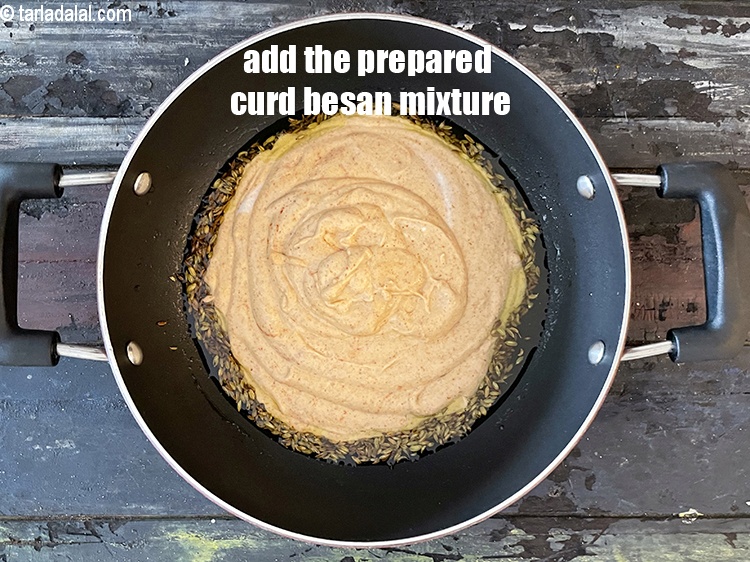 Step 27 – When the seeds crackle, add the curds-besan mixture.