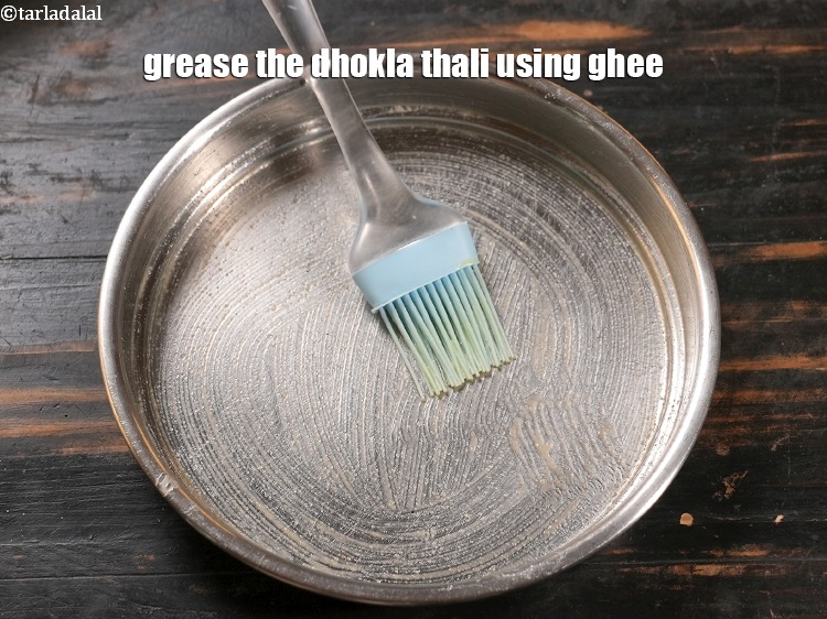Step 23 – Grease the dhokla thali using &frac12; tsp <a href="https://www.tarladalal.com/glossary-ghee-245i">ghee</a>.