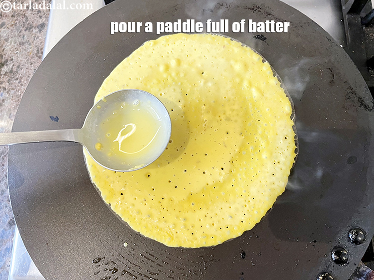 Step 43 – Pour a ladleful of the batter on the tava (griddle) and spread it evenly to …