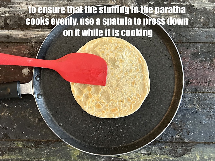 Step 45 – To ensure that the stuffing in the paratha cooks evenly, use a spatula to press …