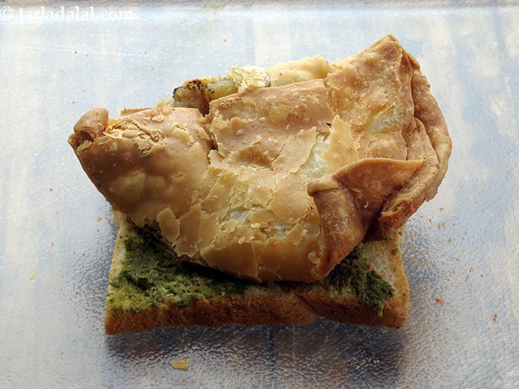 स्टेप 5 – एक समोसे को चपटा करें, इसे एक मक्खन-चटनी वाली ब्रेड …