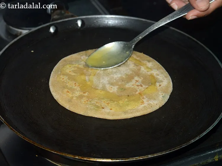 Step 24 – <p>Smear 1 tsp ghee over it. Let the&nbsp;<strong>aloo paratha</strong>&nbsp;cook.</p>