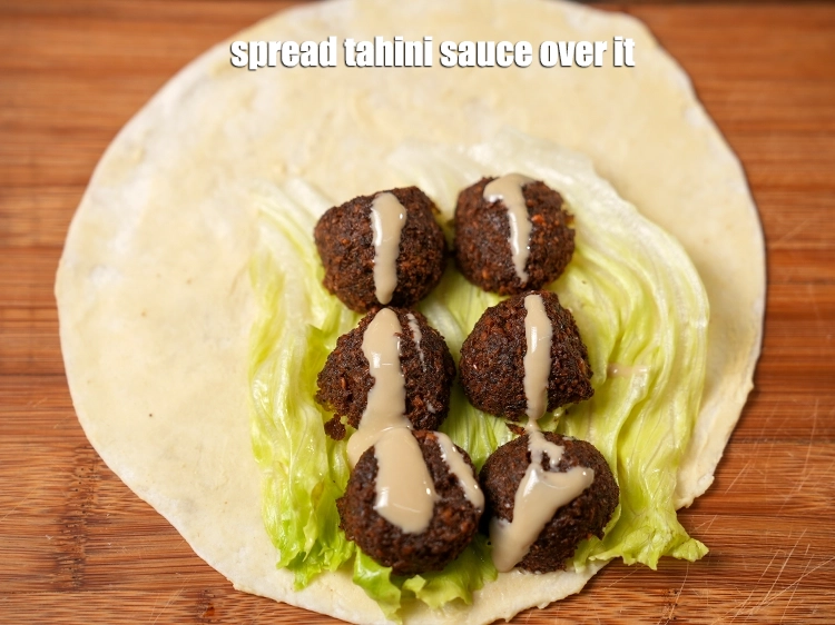 Step 30 – <p><span style="background-color:rgb(255,255,255);color:rgb(0,0,0);">Spread 1 teaspoon of the </span><a href="https://www.tarladalal.com/glossary-tahini-sauce-2408i"><u>tahini sauce</u></a><span style="background-color:rgb(255,255,255);color:rgb(0,0,0);"> over it.</span></p>