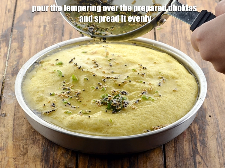 Step 33 – <p>Pour the tempering over the prepared <strong>dhoklas</strong> and spread it evenly. Make sure the dhoklas …