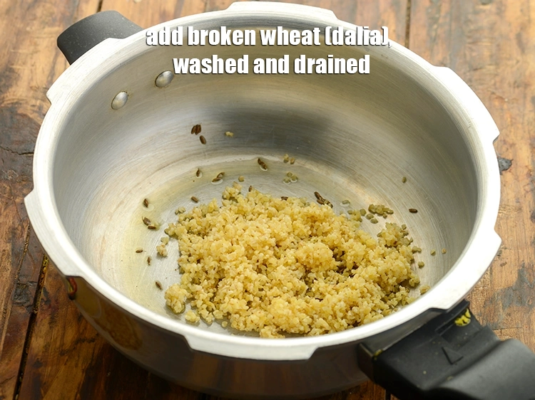 Step 12 – <p>When the cumin seeds crackle, add the <span style="background-color:rgb(255,255,255);color:rgb(0,0,0);">2 tbsp. </span><a href="https://www.tarladalal.com/glossary-broken-wheat-dalia-bulgur-wheat-lapsi-fada-426i"><u>broken wheat (dalia) </u></a><span …