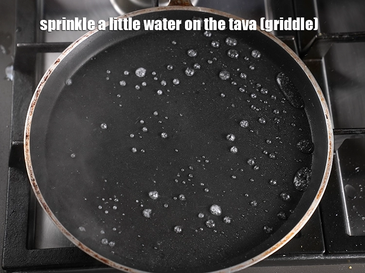 Step 7 – <p><span style="background-color:rgb(255,255,255);color:rgb(0,0,0);">Sprinkle a little <strong>water </strong>on the tava (griddle).</span></p>