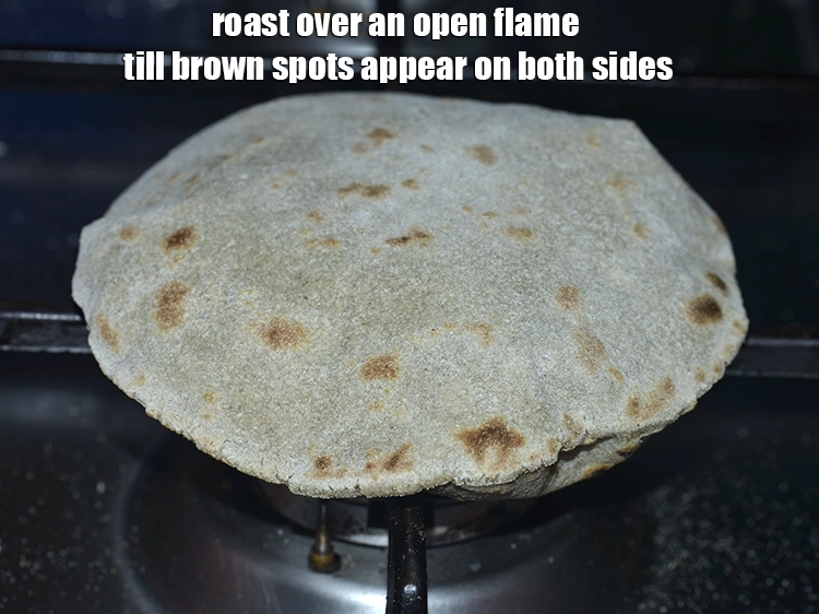 Step 14 – <p>બાજરીના રોટલાને સપાટ ચીપિયા વડે ઉપાડો અને ખુલ્લી આગ પર બંને બાજુ ભૂરા રંગના ડાઘ …