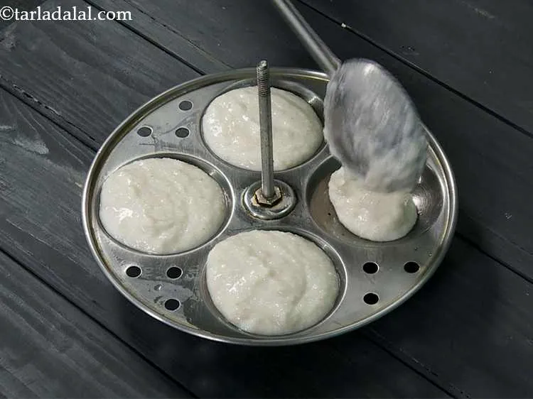 स्टेप 7 – <p>प्रत्येक चुपडे हुए इडली के सांचों में चम्मच भर घोल …
