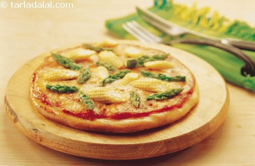 Creamy corn pizza is topeed with pesto flavoured corn sauce and garnished with baby corn and asparagus.